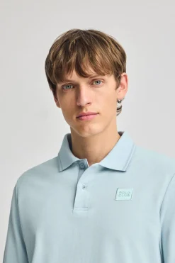 Polo azul claro de manga larga y dos botones con parche logotipado