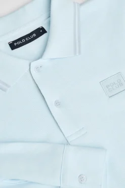 Polo azul claro de manga larga y dos botones con parche logotipado