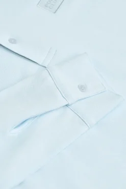 Polo azul claro de manga larga y dos botones con parche logotipado